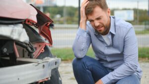 Injured man kneeling beside a damaged car after a collision.