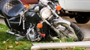 Damaged motorcycle resting on grass near a vehicle after a crash.