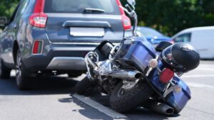 Motorcycle lying on the ground after crashing into a car in traffic.