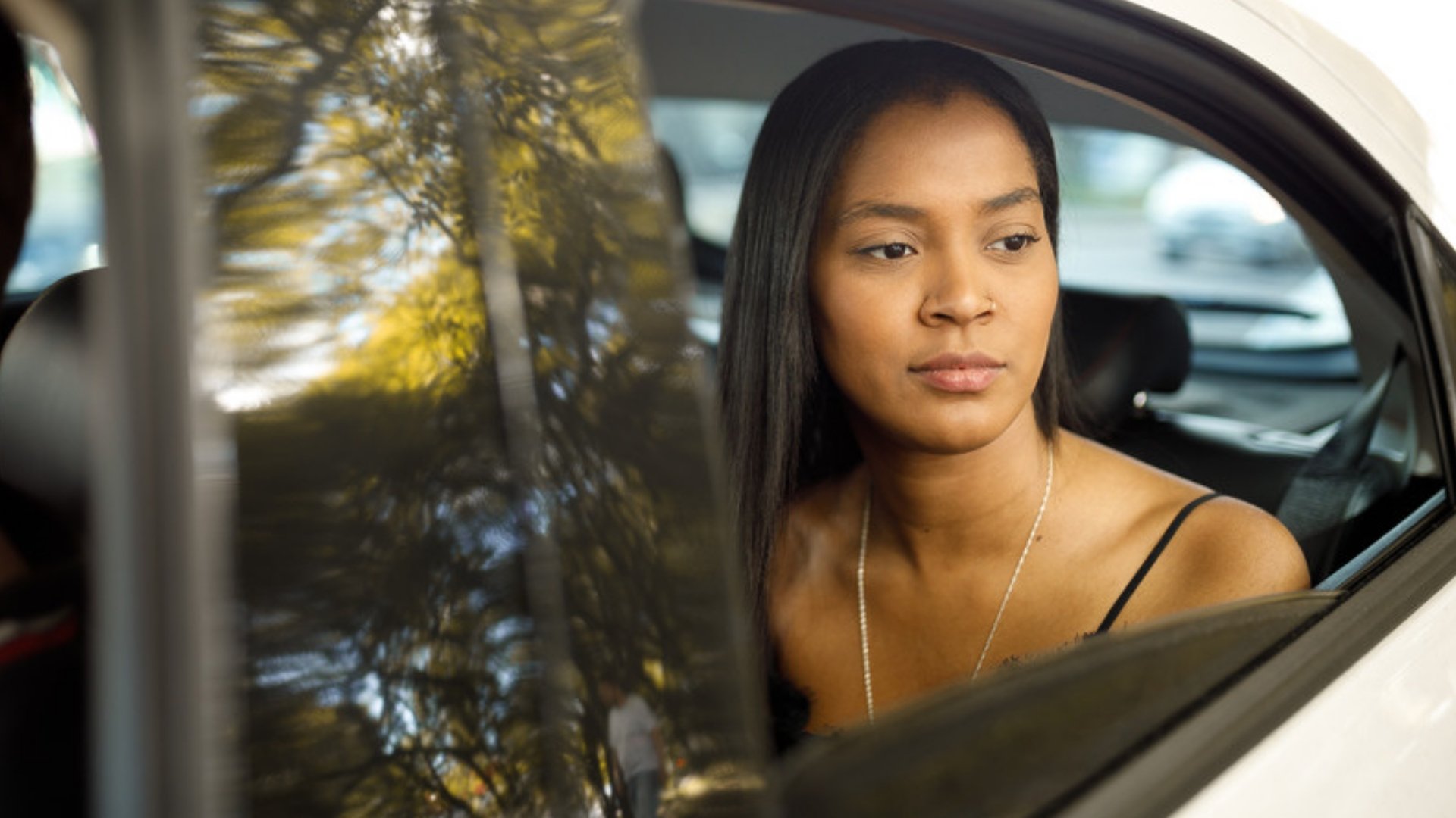A woman sits in the back seat of a white car and looks out the window